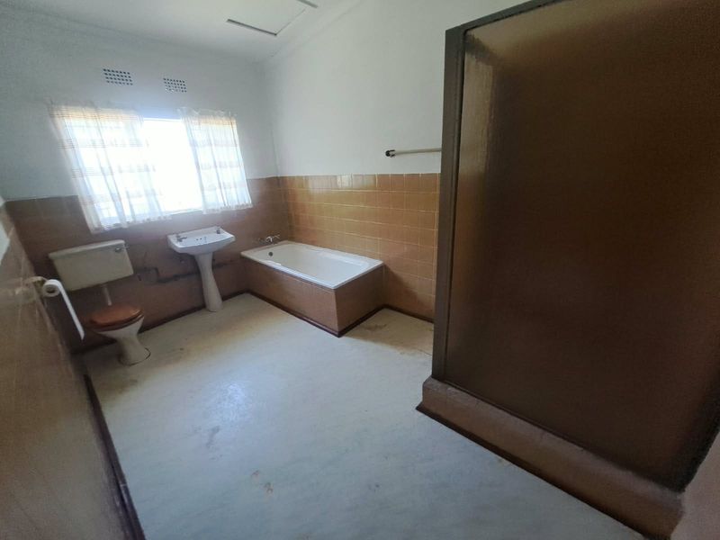 A spacious, dated bathroom featuring a built-in bathtub, separate shower enclosure, pedestal basin, and toilet, with original tiled wall finishes.