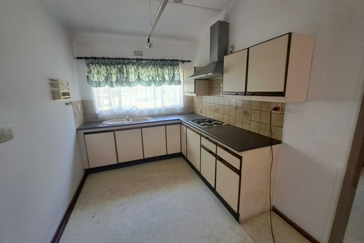 A functional kitchen featuring built-in cabinetry, a gas hob with extractor fan, and a double basin sink, offering a blank canvas for modern updates.