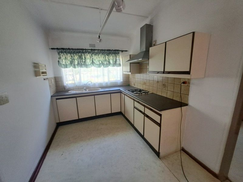 A functional kitchen featuring built-in cabinetry, a gas hob with extractor fan, and a double basin sink, offering a blank canvas for modern updates.