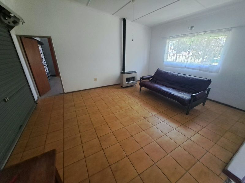 A living area featuring tiled flooring, a built-in fireplace, and a roller shutter door, offering a functional space with potential for cosmetic updates.