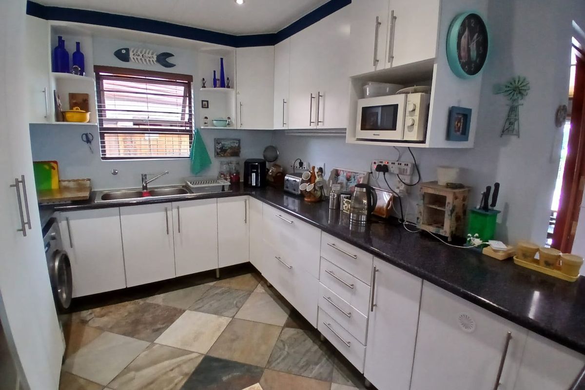 A functional kitchen featuring white cabinetry, dark laminate countertops, a double basin sink, and tiled flooring with integrated microwave space.