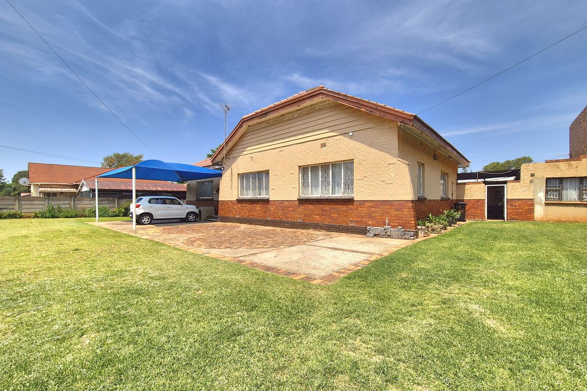 Rear view of a single-story brick house featuring a paved driveway, carport, and a well-maintained lawn area.