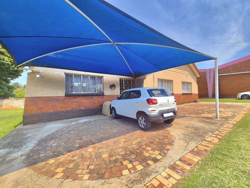 Front exterior view of the house featuring a paved driveway, brick facade, and a large blue shade sail structure.