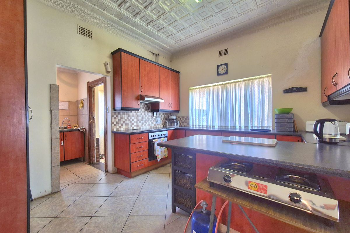 A dated kitchen featuring built-in cabinetry, a pressed metal ceiling, and tiled flooring, with an adjacent scullery area visible through the doorway.