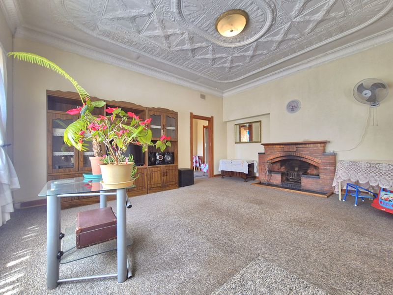 Spacious living room featuring a distinctive ornate pressed metal ceiling and a traditional brick fireplace, offering a classic foundation for modern updates.