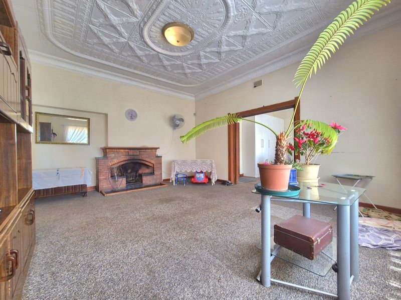Spacious living room featuring a classic brick fireplace and an ornate pressed metal ceiling, offering a traditional aesthetic with potential for modern updates.