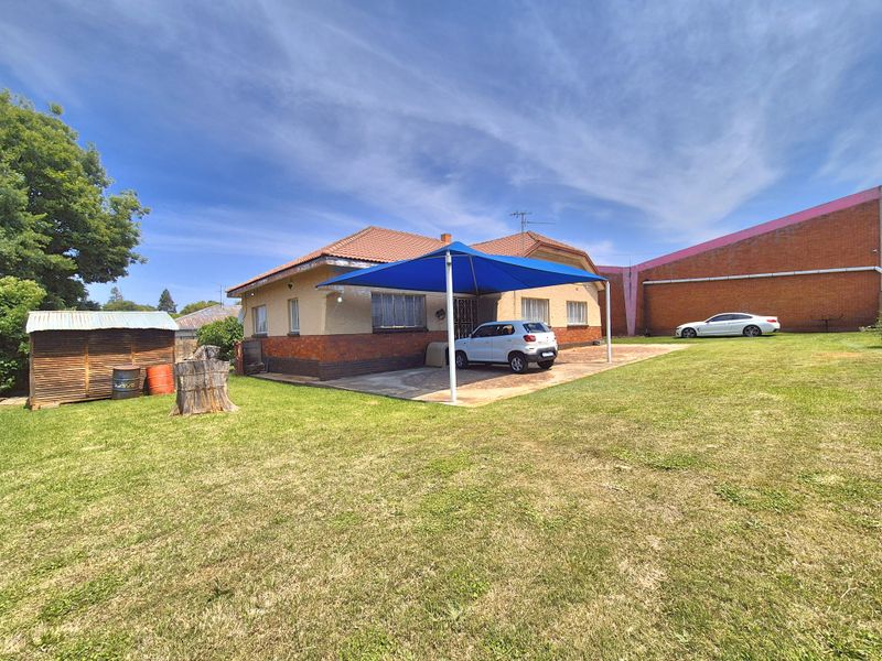 Rear view of the property featuring a brick facade, tiled roof, paved patio area with a shade sail, and a spacious lawn.