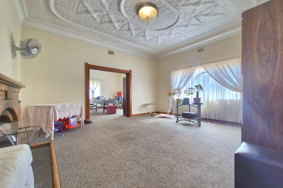 Spacious living room featuring an ornate period plaster ceiling, brick fireplace, and large window, offering a classic foundation for modern updates.