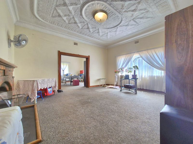Spacious living room featuring an ornate period plaster ceiling, brick fireplace, and large window, offering a classic foundation for modern updates.
