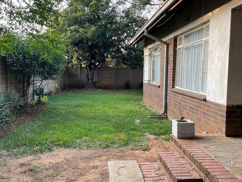 Rear view of the property featuring a brick facade, concrete patio area, and a private garden enclosed by a precast concrete boundary wall.