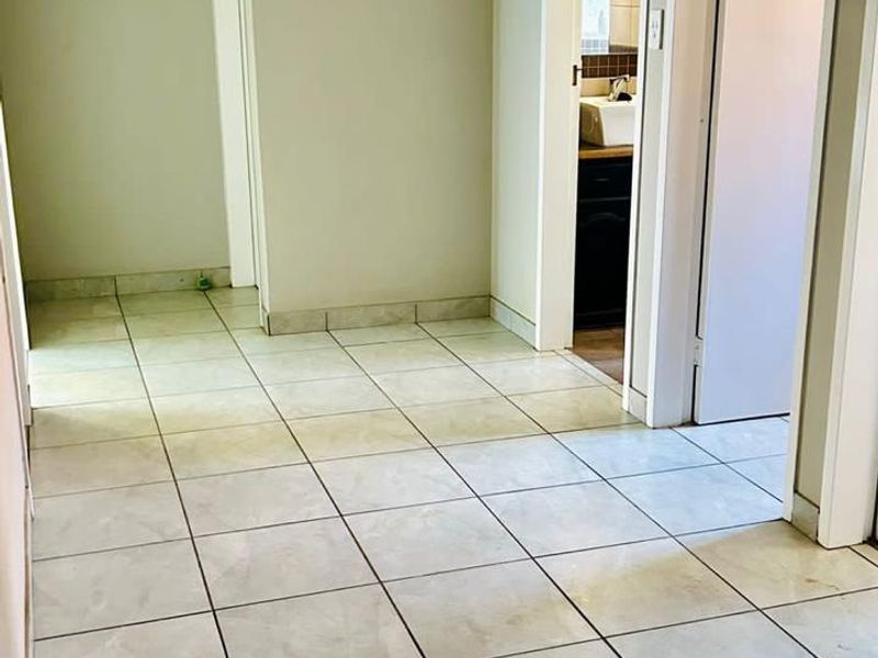 A neutral hallway featuring tiled flooring and access to adjacent rooms, including a glimpse into a bathroom.
