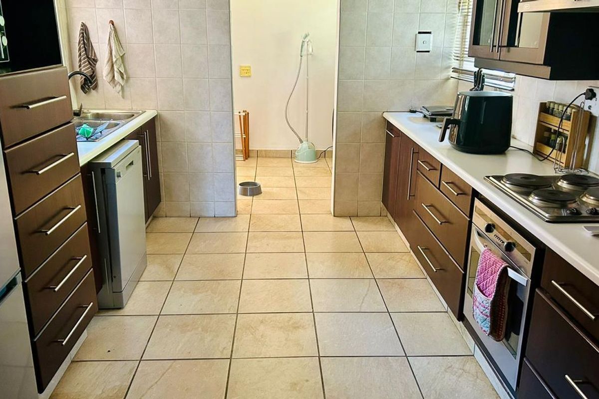 A functional galley-style kitchen featuring dark wood cabinetry, tiled flooring, built-in oven, and electric hob, with an adjacent utility area.