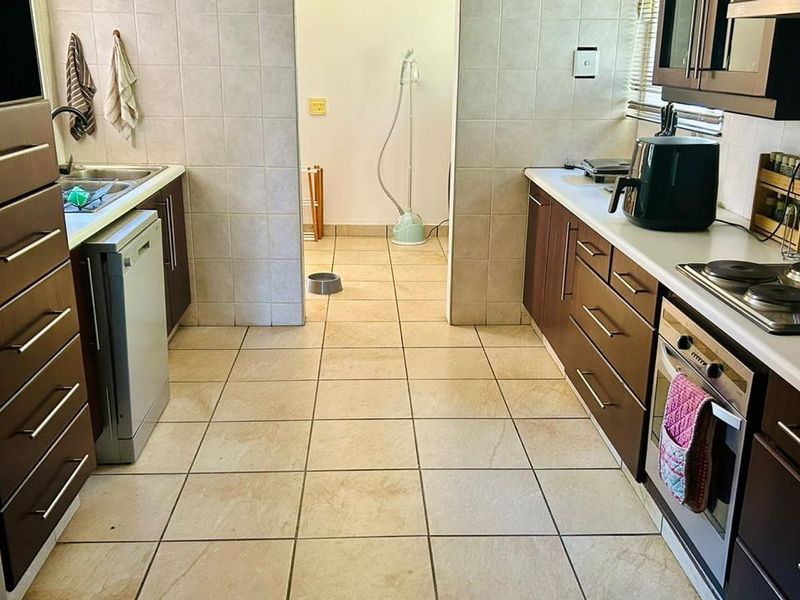 A functional galley-style kitchen featuring dark wood cabinetry, tiled flooring, built-in oven, and electric hob, with an adjacent utility area.