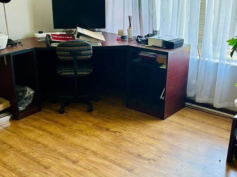 A functional home office space featuring durable laminate wood flooring and a large window that provides ample natural light.