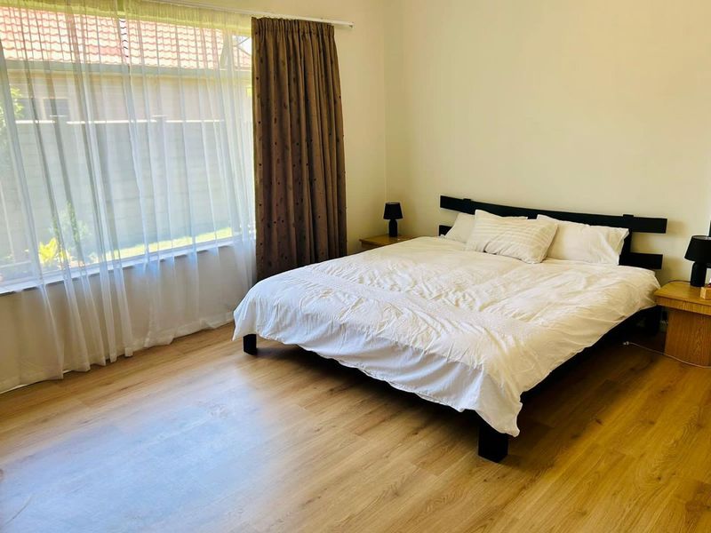 A bright and well-maintained bedroom featuring light-toned laminate flooring and a large window that allows for ample natural light.