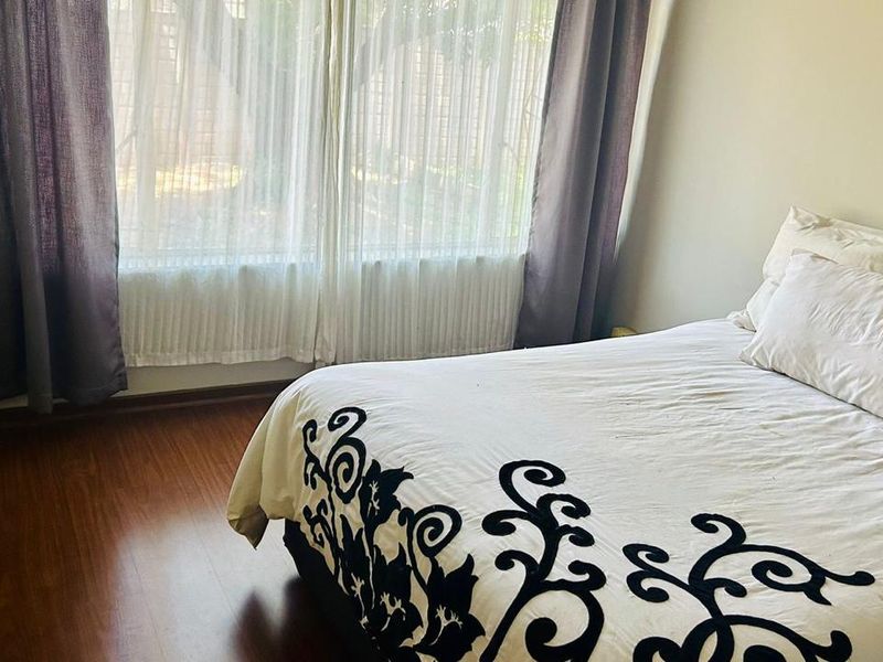 A bedroom featuring laminate flooring and large windows with installed curtain tracks, providing natural light.