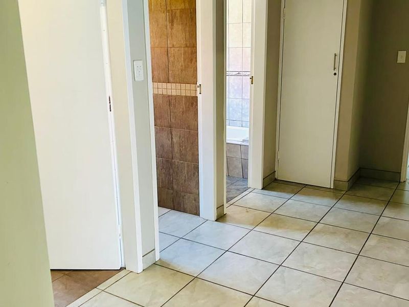 A clean, tiled hallway providing access to multiple rooms, including a bathroom with tiled walls and a built-in storage cupboard.