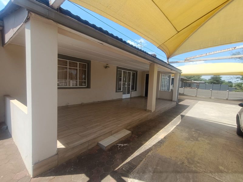 A covered patio area featuring tiled flooring, concrete support pillars, and a large overhead shade sail, providing a functional outdoor entertainment space.