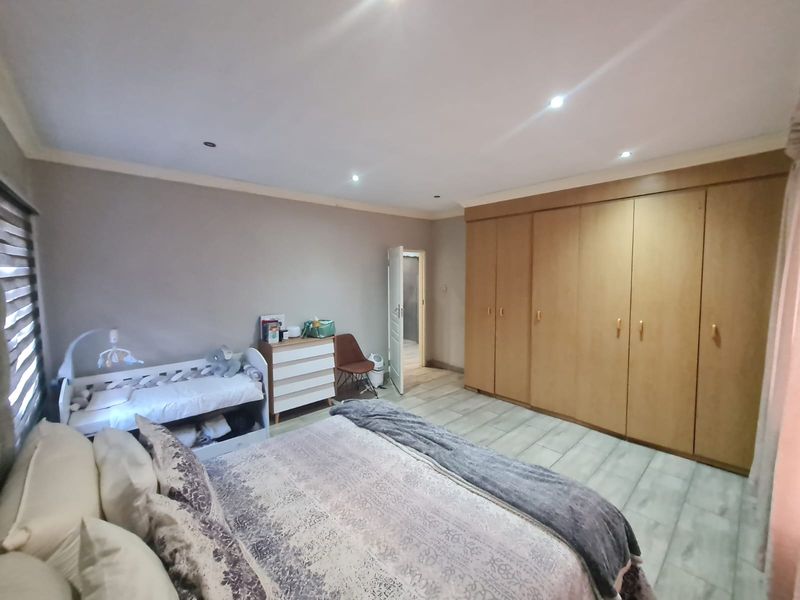 Spacious bedroom featuring extensive built-in wooden cupboards, modern tiled flooring, and recessed downlighting, offering a clean and functional living space.