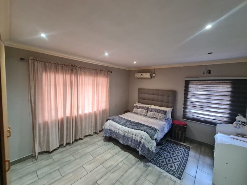 A well-maintained bedroom featuring tiled flooring, recessed downlighting, an integrated air conditioning unit, and neutral wall finishes.