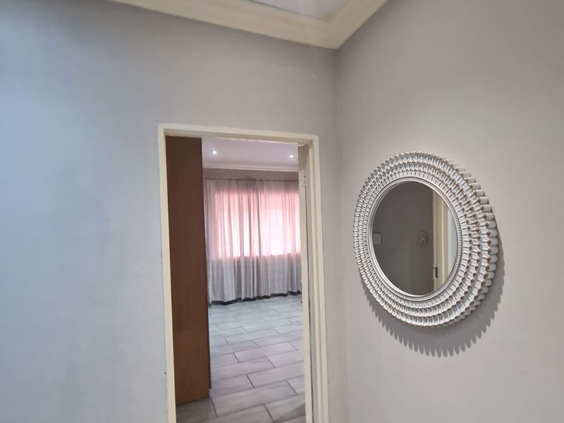 A clean, neutral hallway featuring tiled flooring, recessed downlighting, and coved cornicing, providing a bright transition space between rooms.