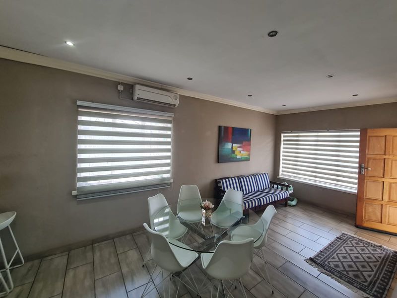 A well-lit living area featuring ceramic floor tiles, recessed downlighting, and a wall-mounted split-system air conditioner with modern zebra blinds.