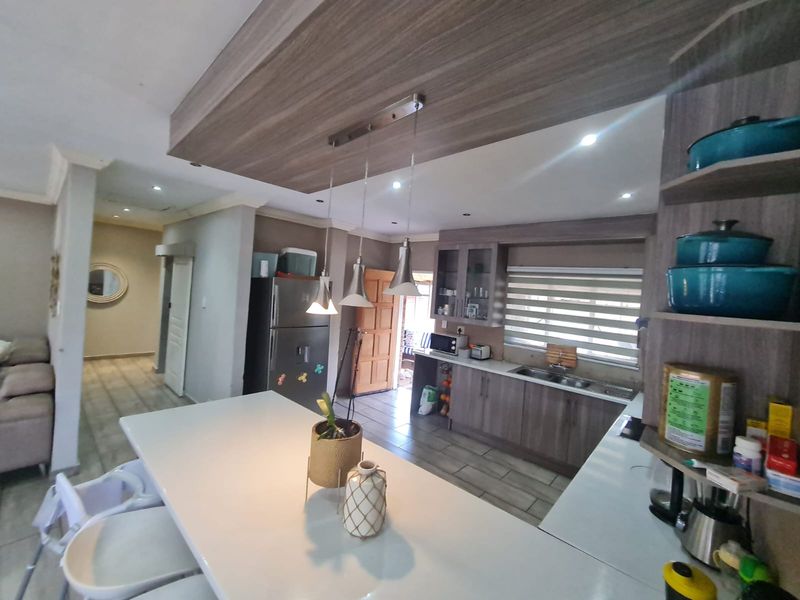 Modern kitchen featuring a central island, wood-finish cabinetry, double sink, and recessed lighting, seamlessly flowing into the adjacent living area.