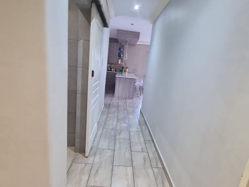 A clean, well-lit hallway featuring modern wood-look tiled flooring, leading towards an open-plan kitchen area.