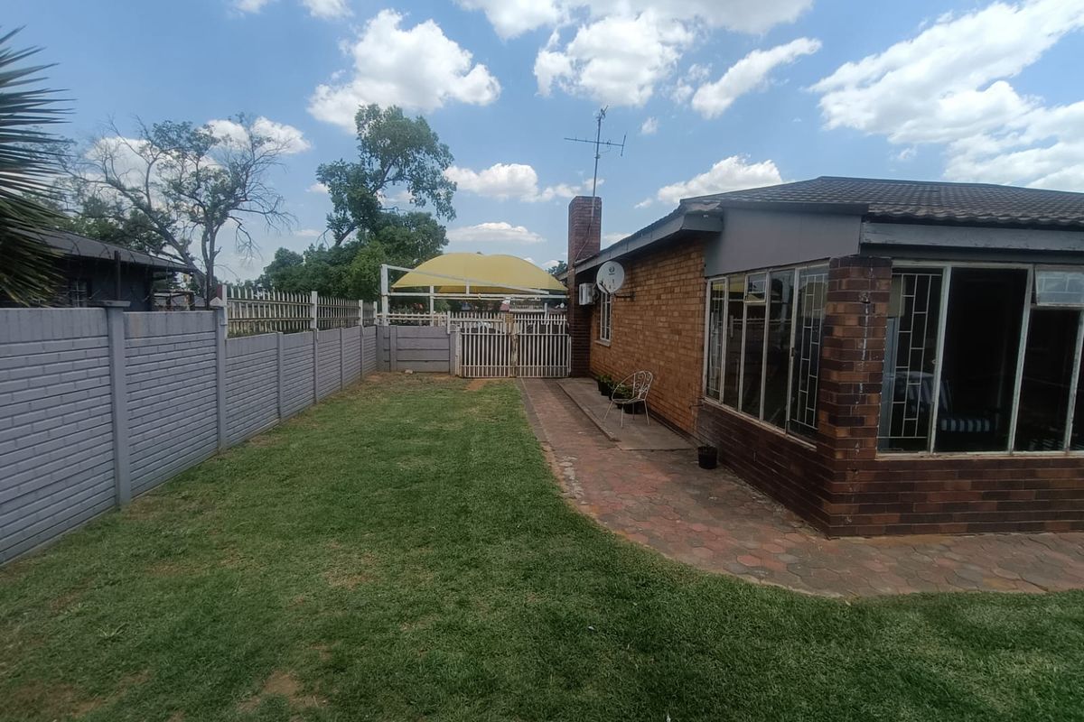 Rear exterior view featuring a brick house, paved patio area, lawn, and secure boundary walling with a shade sail structure.