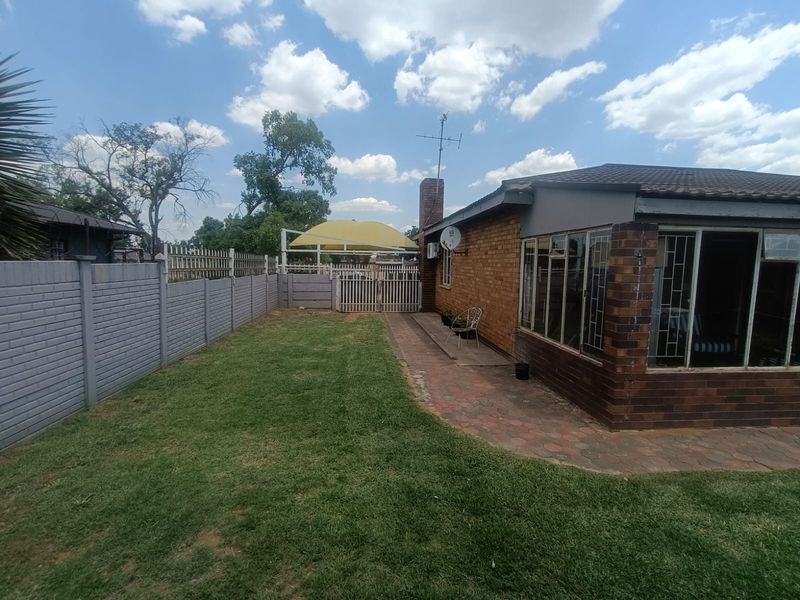 Rear exterior view featuring a brick house, paved patio area, lawn, and secure boundary walling with a shade sail structure.