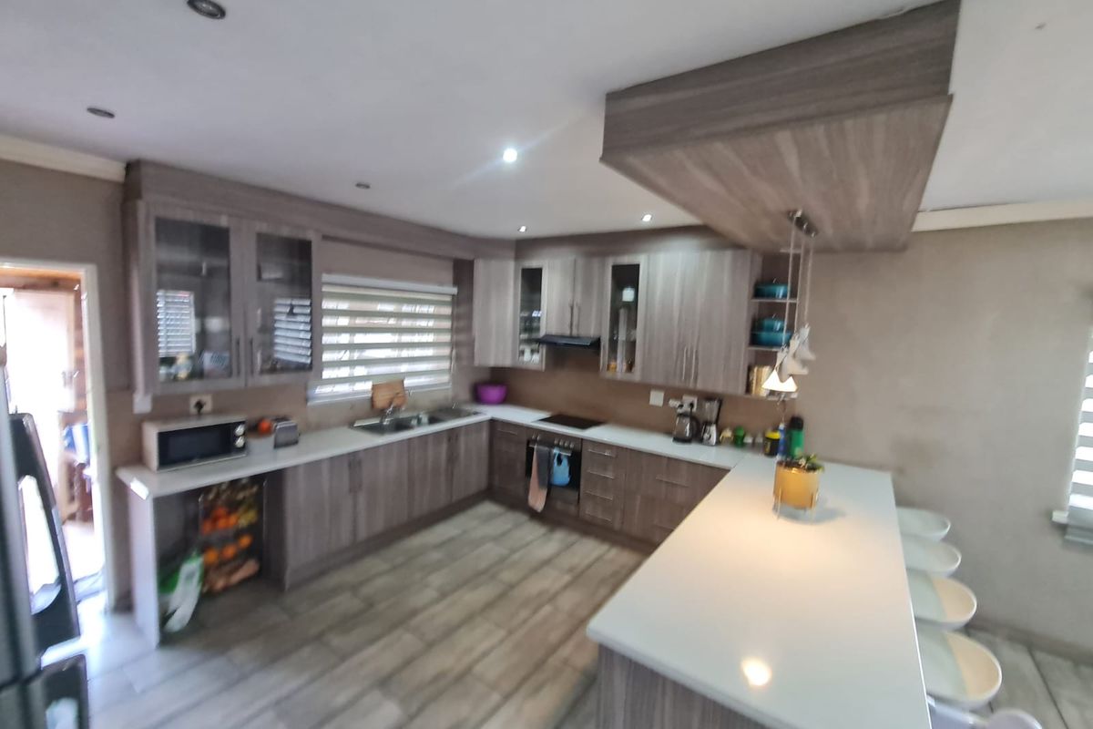 Modern kitchen featuring wood-grain cabinetry, stone countertops, a central island with breakfast bar seating, and integrated appliances.