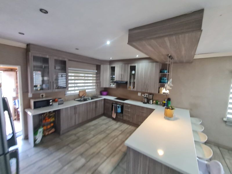 Modern kitchen featuring wood-grain cabinetry, stone countertops, a central island with breakfast bar seating, and integrated appliances.