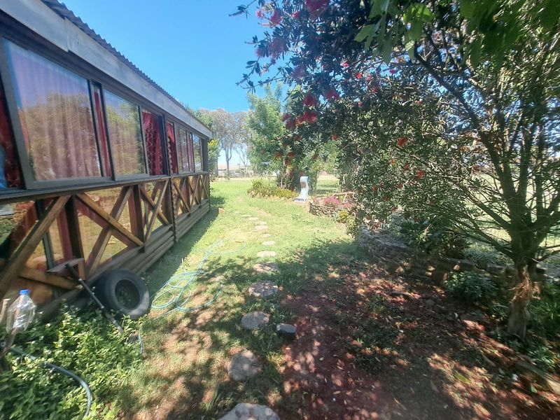 A rear garden view featuring a timber-framed enclosed patio structure, stone pathways, and established landscaping with a stone retaining wall.