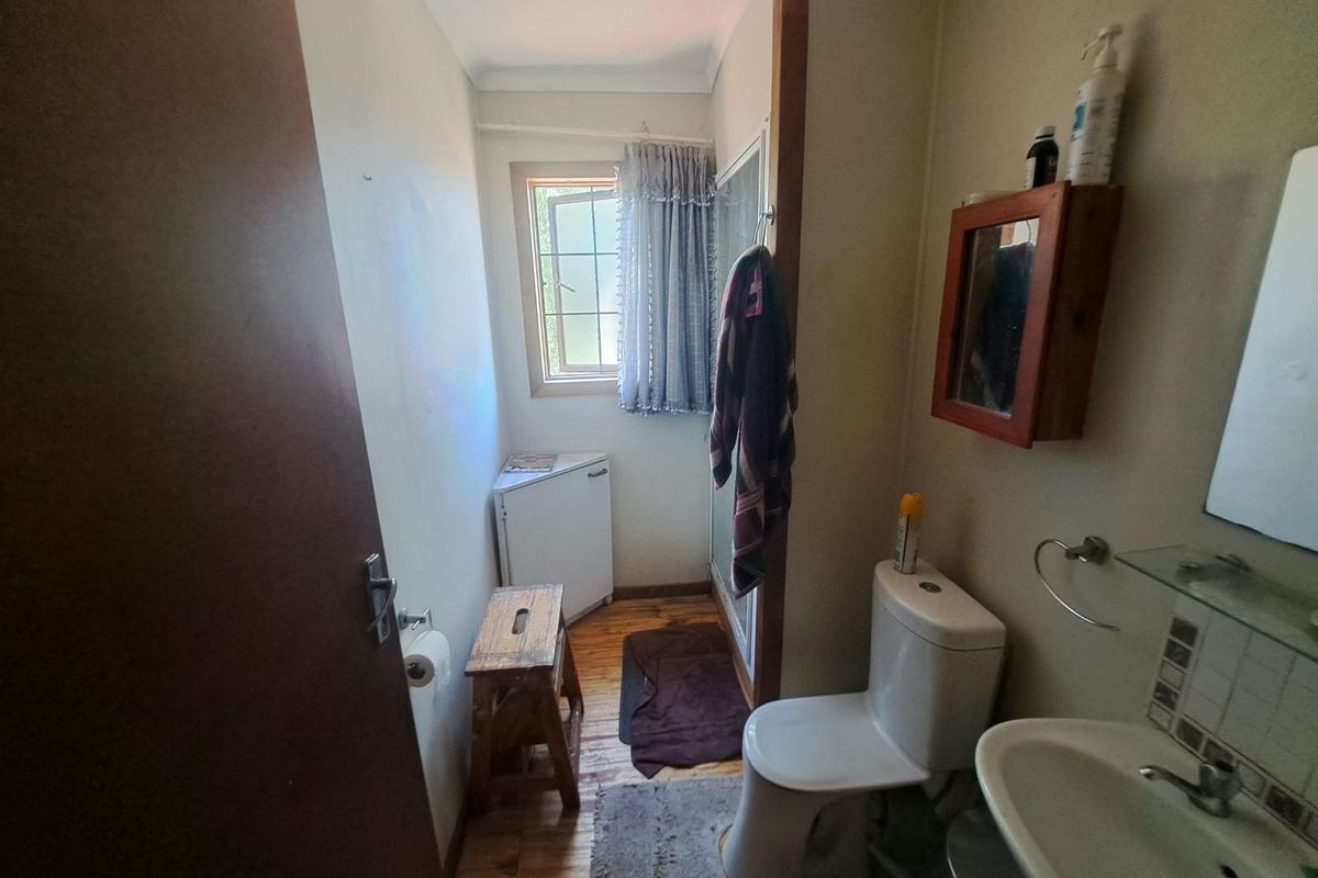 A compact bathroom featuring a toilet, washbasin, and shower enclosure with timber flooring and a window for natural light.