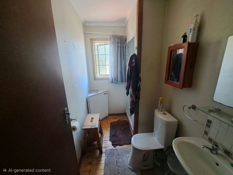 A compact bathroom featuring a toilet, washbasin, and shower enclosure with timber flooring and a window for natural light.