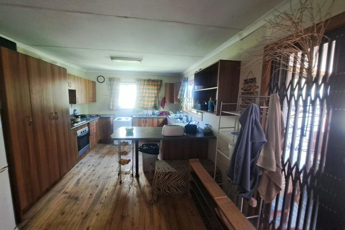 A dated kitchen featuring timber cabinetry, laminate countertops, built-in oven and hob, and timber flooring, offering potential for a modern renovation.