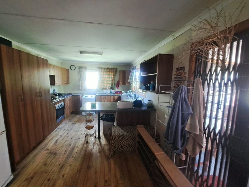 A dated kitchen featuring timber cabinetry, laminate countertops, built-in oven and hob, and timber flooring, offering potential for a modern renovation.