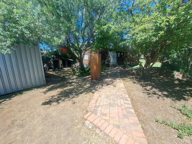 A rear garden area featuring a brick paved pathway leading towards the house, accompanied by a metal storage shed and mature trees.