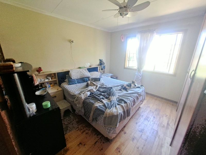 A bedroom featuring timber flooring, a ceiling fan, and a built-in headboard unit. The space requires cosmetic updates to improve its overall condition.