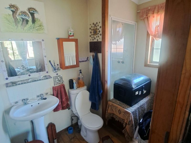 A compact bathroom featuring a pedestal basin, toilet, and shower enclosure with timber flooring, currently requiring cosmetic updates to modernize the space.