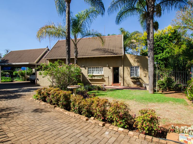 Front view of a duet property featuring a brick driveway, attached carport, tiled roof, and a landscaped front garden with mature palm trees.
