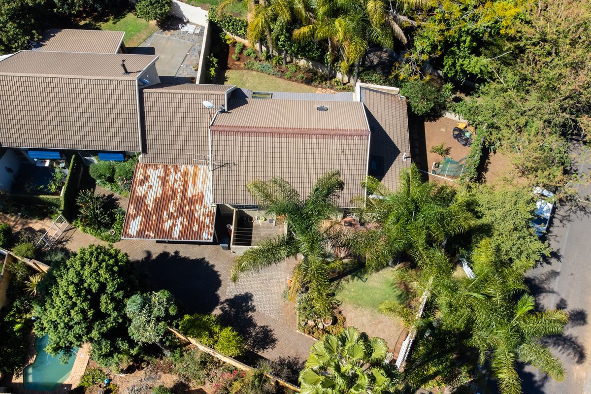 Aerial view of the property showing the tiled roof, paved driveway, swimming pool, and surrounding garden area.