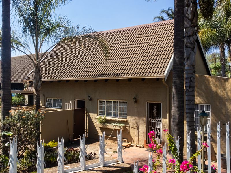 Front elevation of a duet property featuring a tiled roof, paved entrance walkway, and secure perimeter fencing surrounded by established garden landscaping.