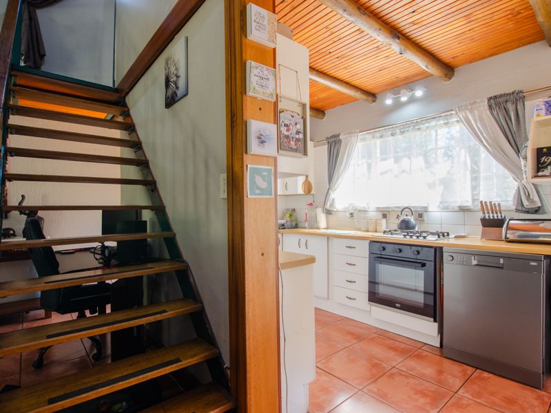 Open plan kitchen area featuring timber ceilings, tiled floors, and a wooden staircase leading to an upper level.