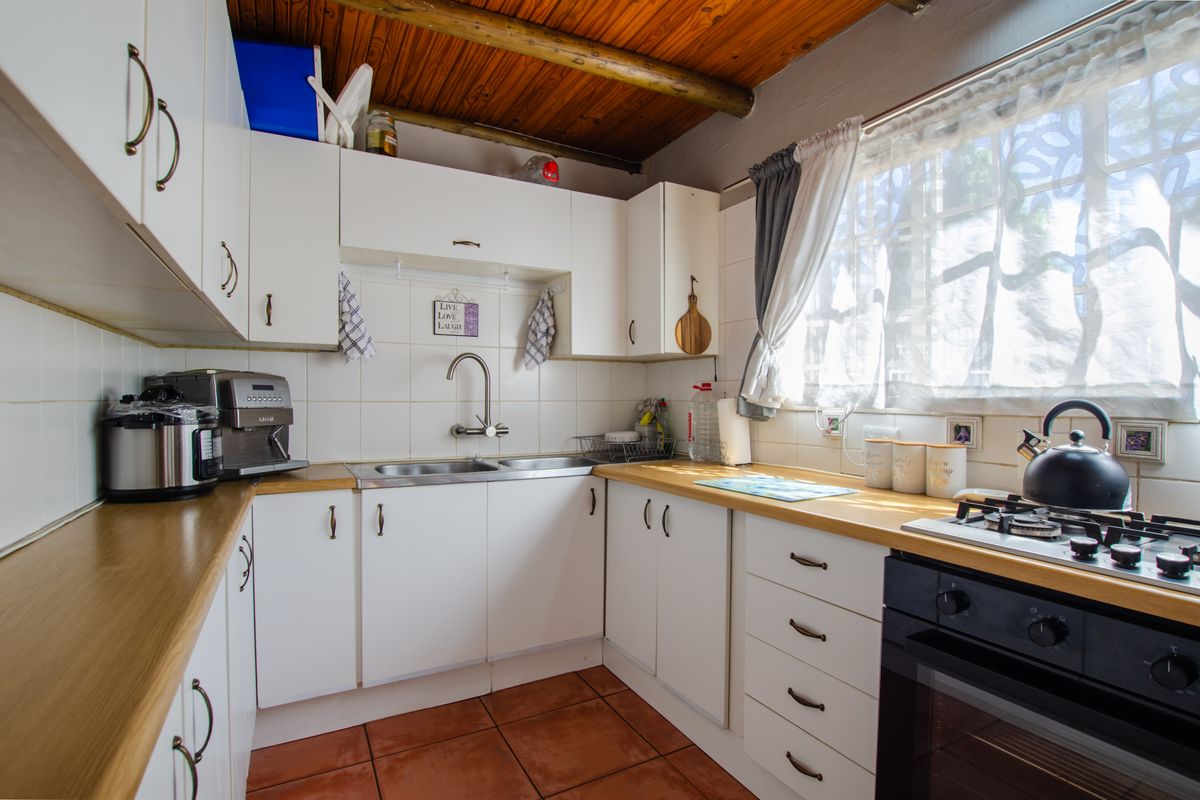 Functional kitchen featuring white cabinetry, laminate countertops, gas hob, built-in oven, and a distinctive exposed timber beam ceiling.