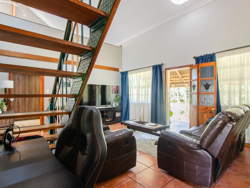 Spacious living area featuring a prominent open-tread timber staircase, vaulted ceilings, tiled flooring, and direct access to the outdoor patio area.