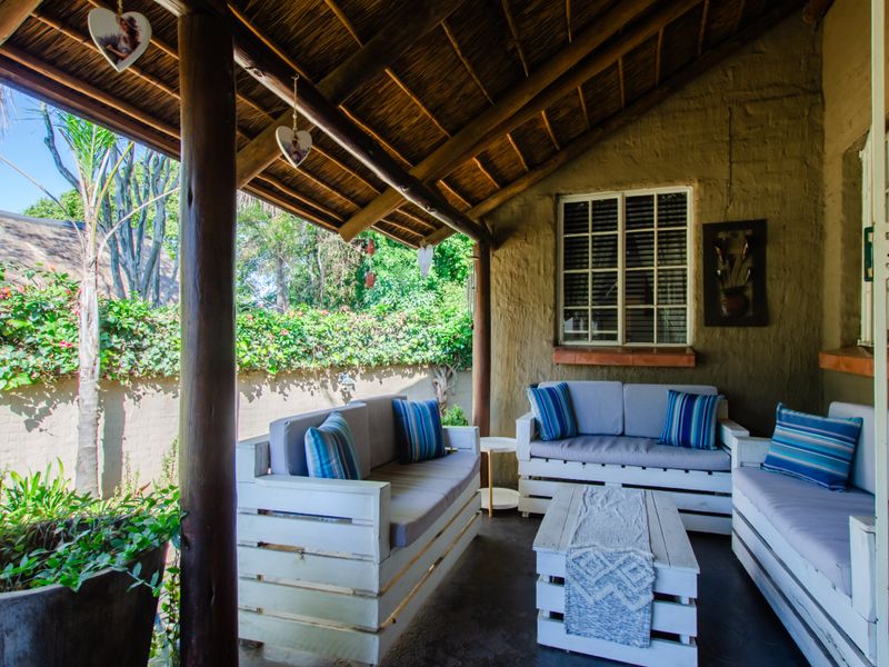 A covered patio area featuring a traditional thatched roof, timber support columns, and a textured masonry wall, providing a rustic outdoor living space.