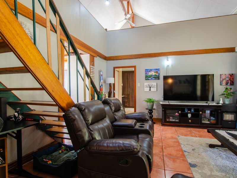 Spacious living room featuring a vaulted ceiling with exposed timber beams, a wooden staircase, and tiled flooring, creating an open and airy atmosphere.