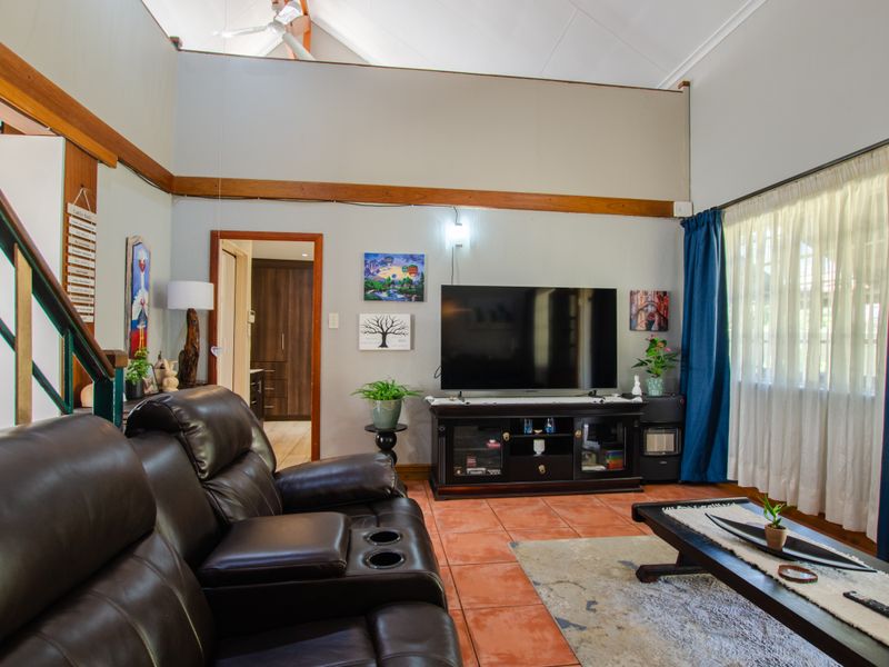 Spacious living room featuring a high vaulted ceiling with exposed timber beams, tiled flooring, and a staircase leading to an upper level.
