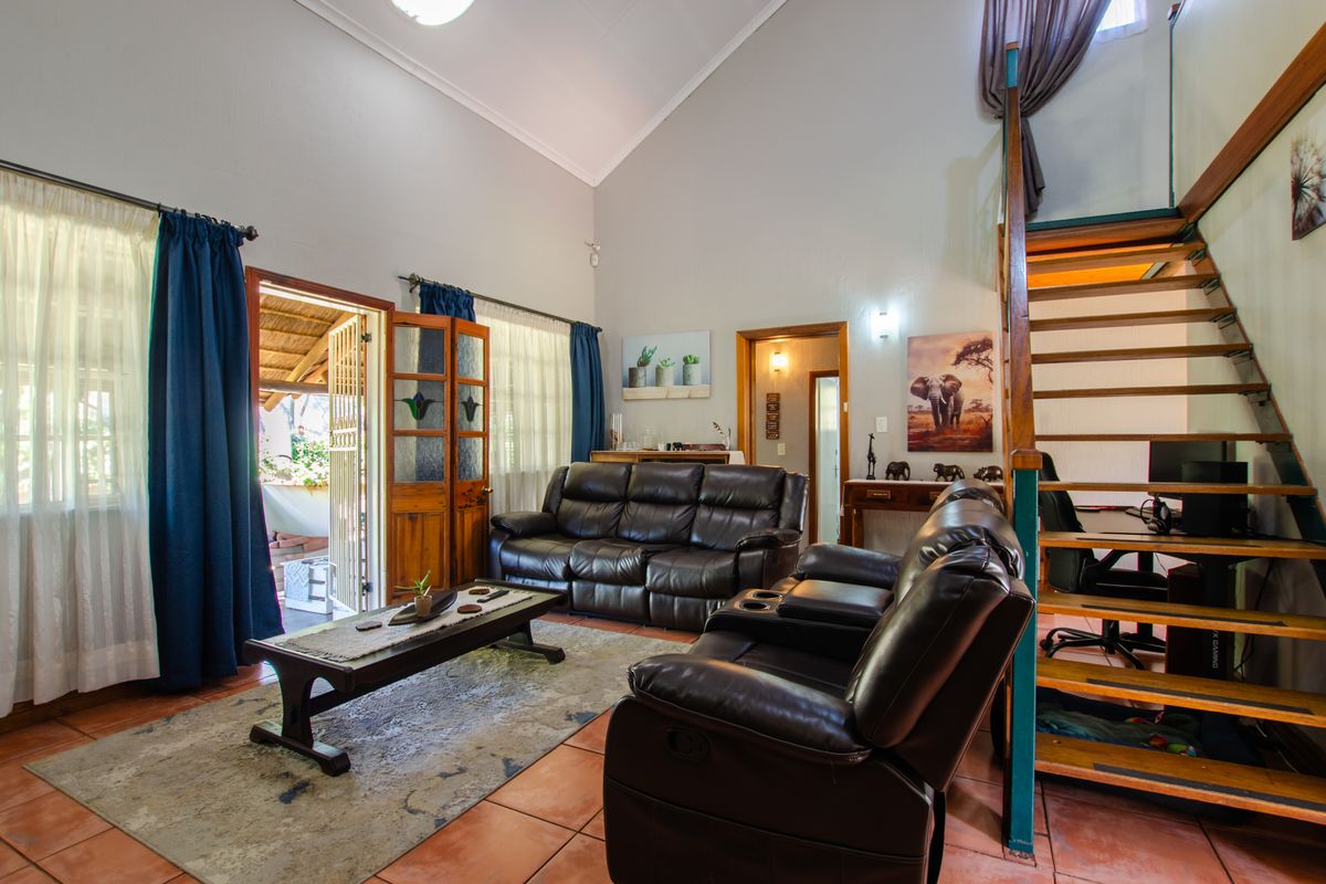 Spacious living room featuring high vaulted ceilings, tiled flooring, and a timber staircase leading to an upper level, with direct access to an outdoor patio.